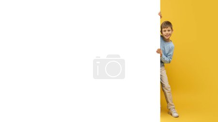 Foto de Joven niño jugando escondido detrás de una gran pancarta blanca en blanco con solo su cara y la mano que muestra - Imagen libre de derechos