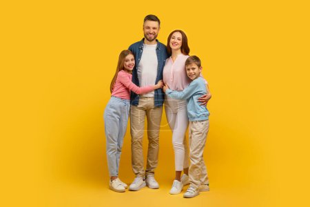 Photo for A happy family of four stands close together with a yellow background, radiating positivity, full length - Royalty Free Image