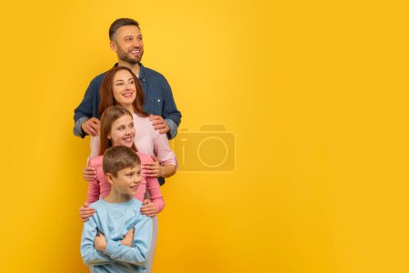 Famille de quatre personnes se tenant à proximité avec une expression heureuse et de contenu sur leurs visages, regardant l'espace de copie