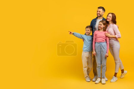 Photo for Smiling family with two kids dressed in casual clothing pointing to something off camera with excitement - Royalty Free Image