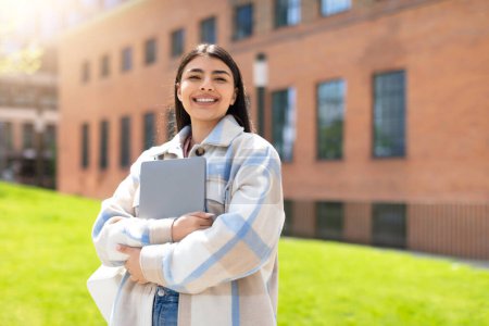 Photo for Delighted student hugs her laptop while standing in an urban park area, looking joyful and satisfied - Royalty Free Image