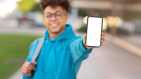 Foto de Fotografía fuera de foco del estudiante brasileño sujetando el teléfono a la cámara, usando gafas y sudadera con capucha azul - Imagen libre de derechos
