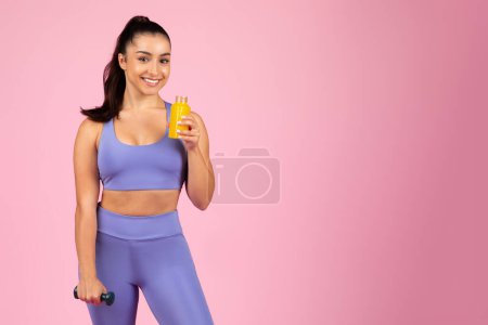 Foto de Fit mujer multitareas con una mancuerna de entrenamiento y jugo de naranja, mostrando un estilo de vida saludable - Imagen libre de derechos