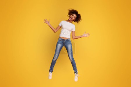 Photo for Hooray. Cheerful african girl jumping in air, orange background - Royalty Free Image