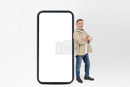 Un hombre mayor alegre está al lado de una gran maqueta de teléfonos inteligentes con una pantalla en blanco listo para el contenido de diseño