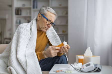Téléchargez les photos : Homme âgé préoccupé tenant une bouteille de pilule, l'examinant de près, ce qui pourrait signifier une gestion de la santé ou une routine médicale - en image libre de droit