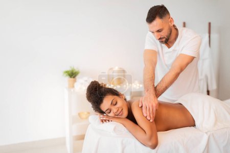 Téléchargez les photos : Une scène relaxante avec une femme afro-américaine recevant un massage du dos dans un cadre spa serein, espace de copie - en image libre de droit