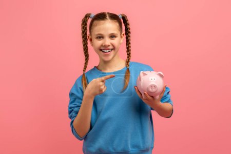 A smiling girl pointing to a piggy bank, symbolizing the importance of savings and financial awareness on a pink background