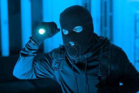 Une scène mystérieuse mettant en scène une personne dans un masque tenant une lampe de poche, avec un grade de couleur bleu lourd