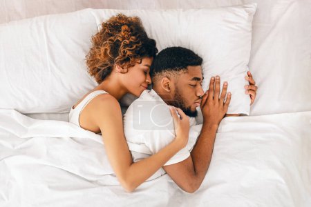 Téléchargez les photos : Femme noire étreignant son homme et souriant, jouissant du sommeil ensemble au lit, vue de dessus avec espace vide - en image libre de droit