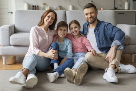 Téléchargez les photos : Une famille joyeuse de quatre parents et enfants assis ensemble sur le sol posant pour une photo dans un cadre familial - en image libre de droit