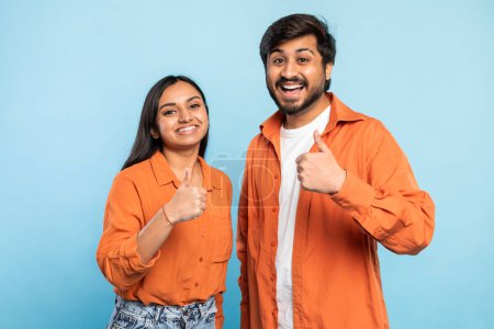 Couple indien souriant donnant les pouces à la caméra, exprimant son approbation et sa positivité sur un fond bleu