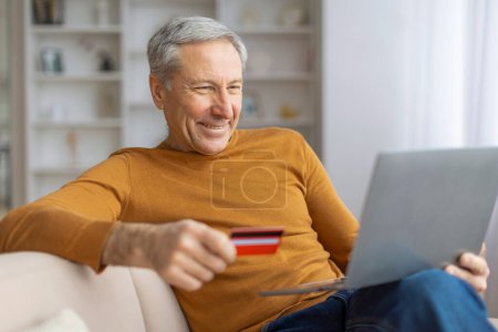 Photo for Senior gentleman with a laptop and credit card smiles as he enjoys the convenience of online shopping - Royalty Free Image