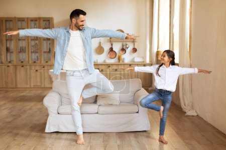 Téléchargez les photos : Père et fille trouvent un équilibre ludique posent ensemble dans un salon, mettant en valeur leur relation amusante - en image libre de droit