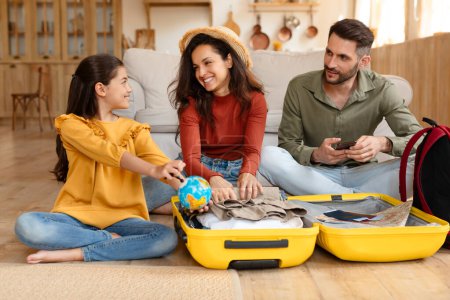A family of three smiles and enjoys each others company while packing a suitcase, preparing for a holiday