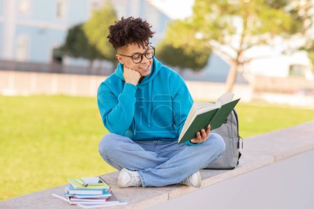 Foto de Joven brasileño en ropa casual se sienta al aire libre pensando profundamente mientras sostiene un lápiz y un cuaderno para notas - Imagen libre de derechos