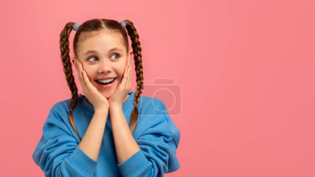Photo for A joyous girl with hands on her cheeks shows excitement and happiness on a pink backdrop, copy space - Royalty Free Image