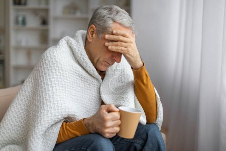 A senior man with silver hair holds a mug while displaying a seemingly troubled or contemplative expression, indicating concern or illness