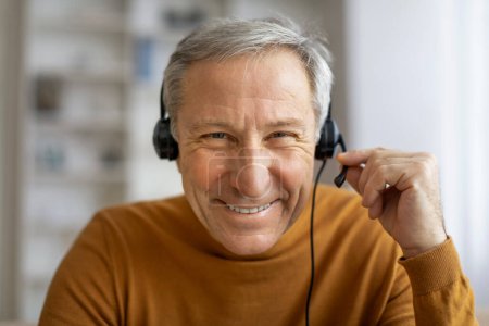 An older gentleman with a content smile wearing large headphones, businessman have video conference