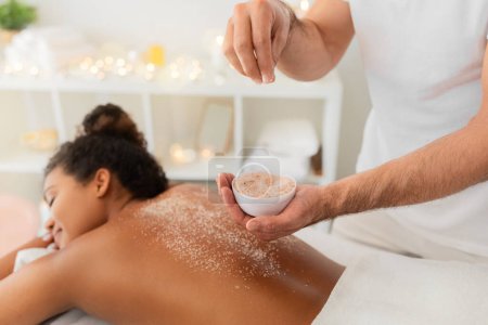 Hands pouring salt scrub on african american woman back during an exfoliating spa session at saloon