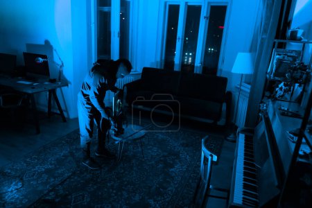 A solitary burglar is caught mid-action, cutting into a floor as part of a heinous crime, under a dimly lit environment