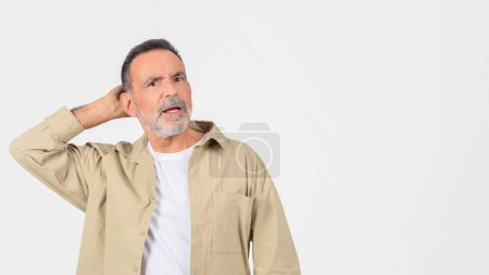 Foto de Hombre mayor desconcertado rascándose la cabeza en un gesto de confusión u olvido sobre un fondo blanco - Imagen libre de derechos