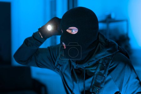 An intense scenario with a person wearing a balaclava using a flashlight, possibly for a crime scene
