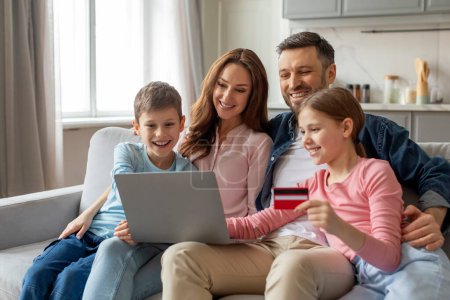 Una familia de cuatro se dedica a las compras en línea como uno de los niños tiene una tarjeta de crédito mientras mira un ordenador portátil