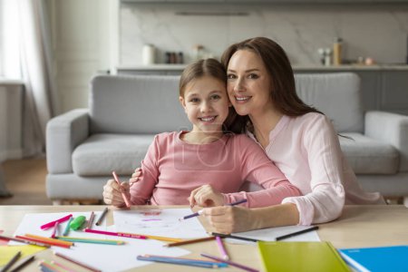 Photo for A happy mother and her young daughter sit at a table filled with colored pencils, both smiling and looking at the camera while engaging in a creative activity - Royalty Free Image
