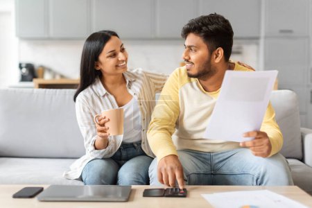 Photo for Indian man and woman are seated on a couch, both deeply engrossed in examining a piece of paper placed on their laps, happy couple checking documents - Royalty Free Image