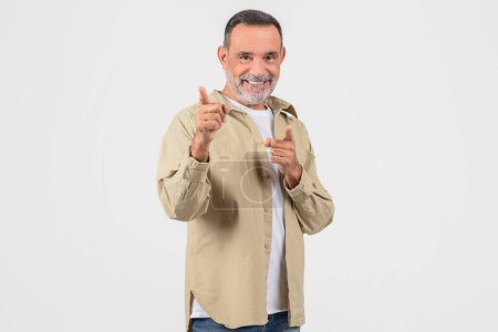 Fröhlicher älterer Mann, der selbstbewusst mit beiden Händen in die Kamera zeigt und auf weißem Hintergrund Auswahl oder Auswahl vorschlägt