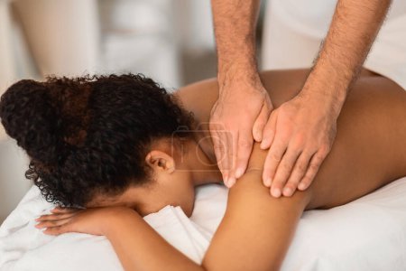 Téléchargez les photos : Image détaillée de la femme afro-américaine recevant un massage des tissus profonds se concentrant sur son omoplate - en image libre de droit