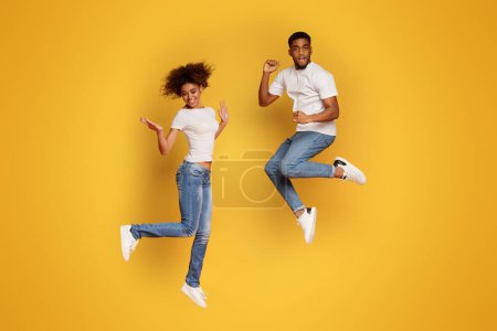 Photo for Carefree african american man and woman jumping in air, orange studio background - Royalty Free Image