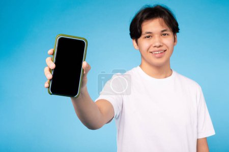 Cheerful young asian guy holding out a mobile phone with screen visible for technology representation