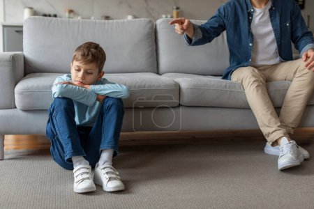 Photo for A dejected young boy sits on the floor with crossed arms and bowed head, evoking a feeling of sadness or punishment in a home environment - Royalty Free Image