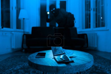 Photo for An intruder swiftly collects valuables, a wallet and phone illuminated by a flashlight, portraying theft in a domestic setting - Royalty Free Image