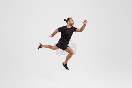 Hombre enérgico en ropa deportiva capturado a media zancada, que ilustra el movimiento y la vitalidad en una pose dinámica sobre fondo gris