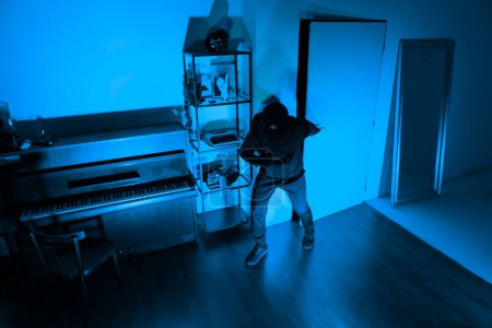 Photo for Stealthy burglar wearing dark clothing and a ski mask, using a crowbar to unlawfully enter a home - Royalty Free Image