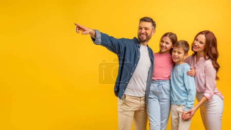 Téléchargez les photos : Charmante famille suit comme le père souligne quelque chose d'intéressant sur un fond jaune vif - en image libre de droit