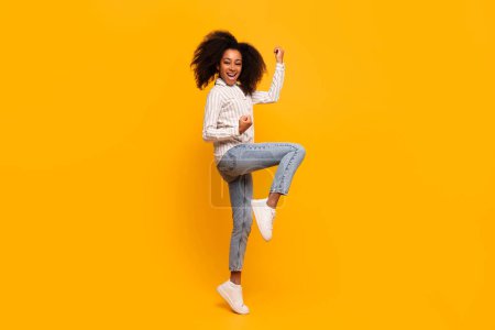 Téléchargez les photos : Femme afro-américaine extatique avec des cheveux bouclés dansant et s'amusant sur un fond jaune - en image libre de droit