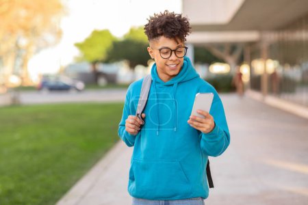 Casual young brazilian guy student checking smartphone, wearing glasses and blue hoodie, with blurred background