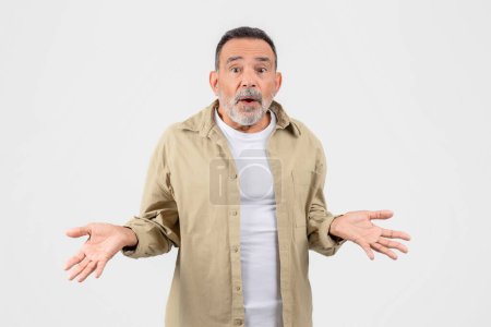 Photo for An older man with a beard looks surprised and confused, shrugging with his hands up in a gesture of uncertainty - Royalty Free Image