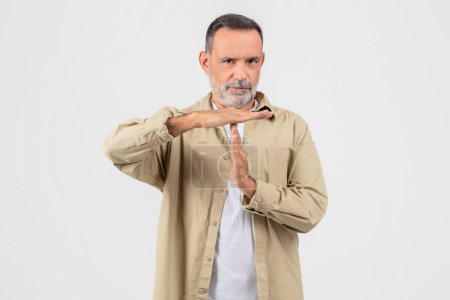 A mature man with a beard in casual attire making a time out or pause gesture with his hands against a white background