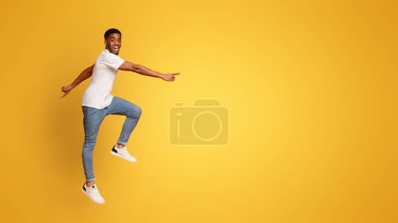 Téléchargez les photos : Homme afro-américain excité marchant dans les airs, fond de studio orange avec espace vide - en image libre de droit
