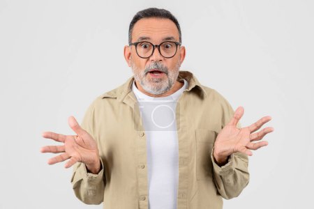 Photo for Elderly man with glasses expressing surprise or disbelief, with open hands and a shocked facial expression - Royalty Free Image