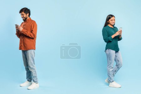 Hindu man and woman stand distantly on opposite ends of the frame, each absorbed in their smartphone on a blue backdrop