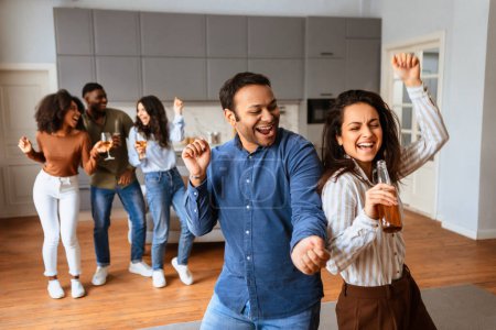Energetic multiracial friends having fun dancing together in a home setting with drinks in their hands, expressing joy