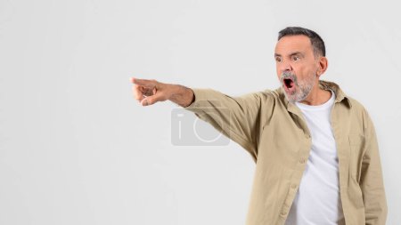 Astonished older man pointing with one hand, mouth open in shock on a clear white background, copy space