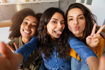 Verspielt und lebhaft machen drei multiethnische Freundinnen ein Selfie und halten einen Moment des Glücks und der Freundschaft mit ausdrucksstarken Gesichtern fest