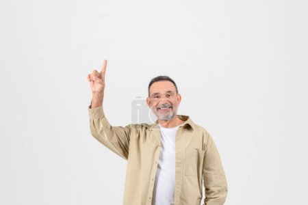 Foto de Alegre hombre mayor sonriente apuntando hacia arriba con un brazo, emocionado por algo de arriba sobre fondo blanco llano - Imagen libre de derechos